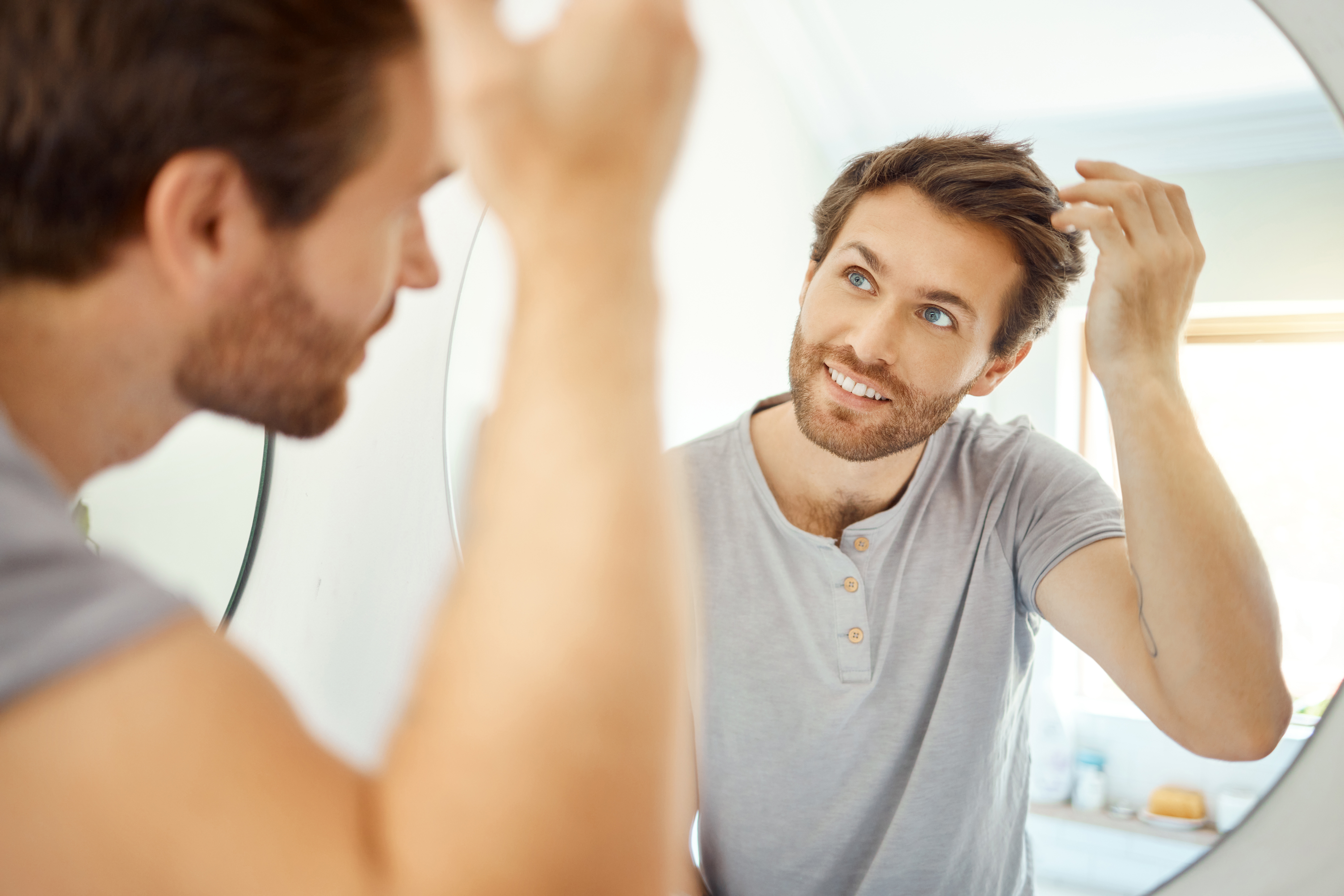 Young man styling his hair while looking in a bathroom mirror